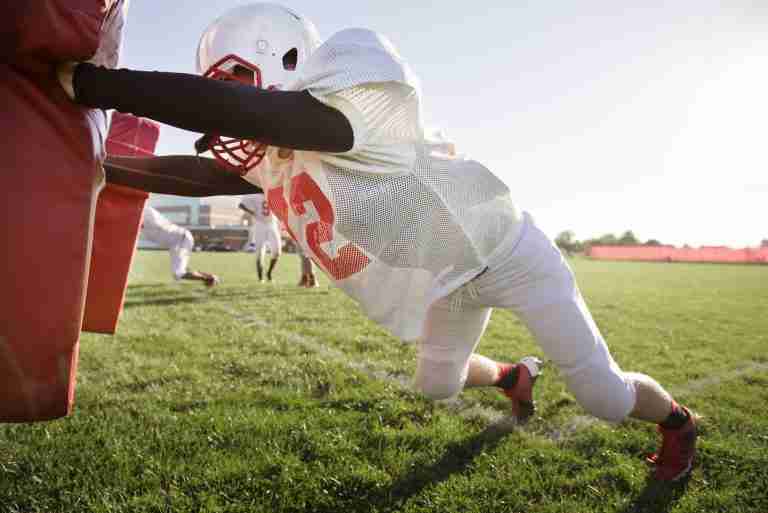 American Football Player Pushing Football Sled On Field